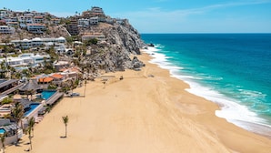 A coastal hotel with a beach view, multiple pools, and a rocky cliff backdrop.