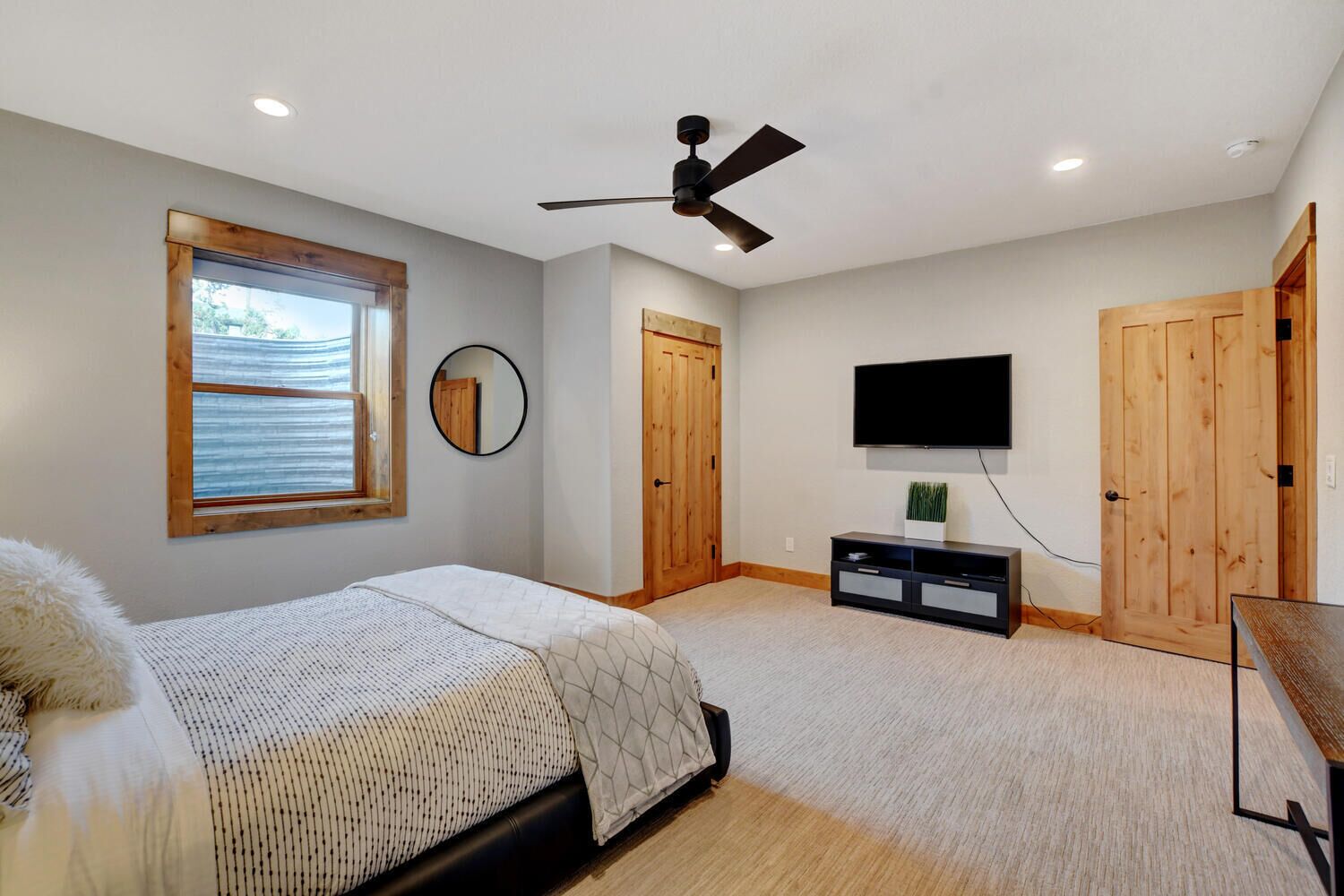 Un dormitorio con cama, ventilador de techo, televisor y puertas de madera.