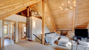Une pièce mansardée spacieuse avec un plafond haut, un escalier intégré, une grande fenêtre et un coin salon confortable avec un téléviseur à écran plat.
