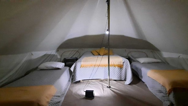 Una carpa con dos camas, cada una con almohadas y mantas, y una cama central con una manta.