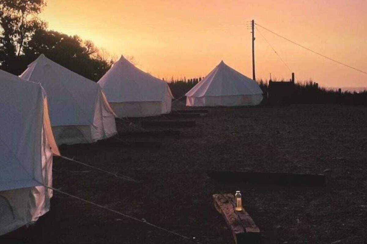 Rivi valkoisia teltoja leirintäalueella, taustalla auringonlasku.
