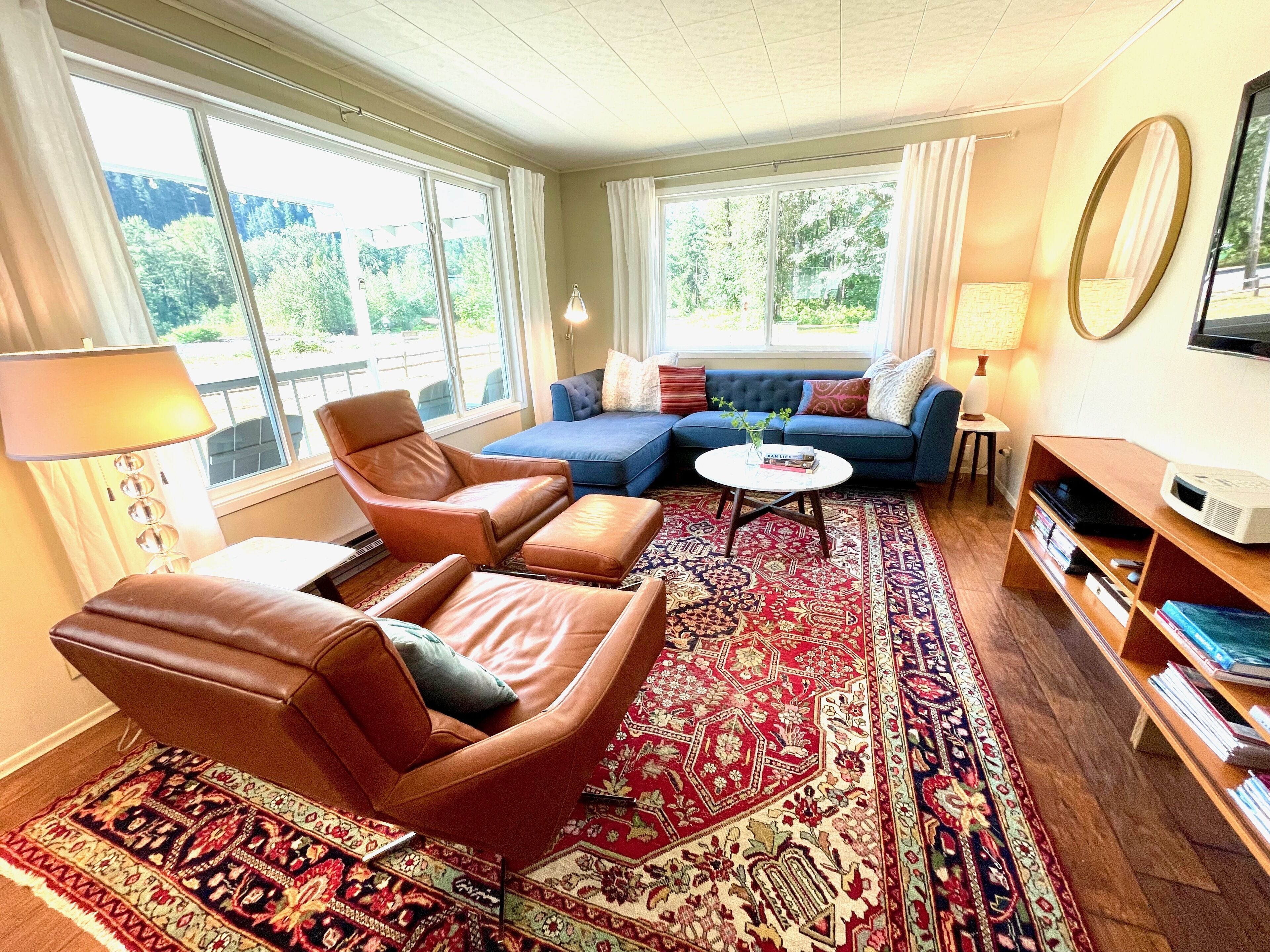 A living room with a brown leather sofa, a blue sectional, a coffee table, and a large window with curtains.