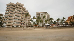 Un hotel frente a la playa con varios pisos, palmeras y sombrillas.