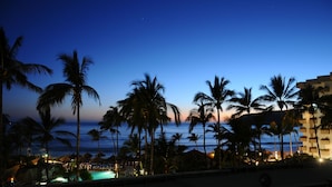 Un resort con piscina, palmeras y vista al océano al anochecer.