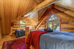 Un dormitorio tipo cabaña de madera con cama en altillo, una manta roja y suelo de madera.