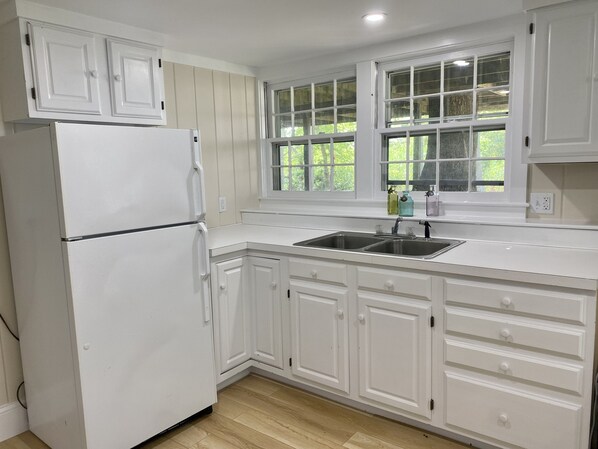 A kitchen with white cabinets, a double sink, and a refrigerator. - Spacious deck with amazing view, neighborhood path to Skaket Beach, game room (Orleans)