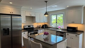 A modern kitchen with stainless steel appliances, a central island, and a large window providing natural light. - Spacious deck with amazing view, neighborhood path to Skaket Beach, game room (Orleans)