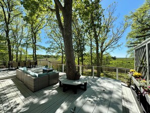 A wooden deck with outdoor seating, surrounded by trees and a clear view of the landscape. - Spacious deck with amazing view, neighborhood path to Skaket Beach, game room (Orleans)