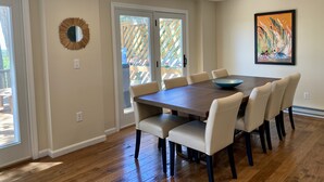 A dining area with a large wooden table, six chairs, a decorative mirror, and a painting on the wall. - Spacious deck with amazing view, neighborhood path to Skaket Beach, game room (Orleans)