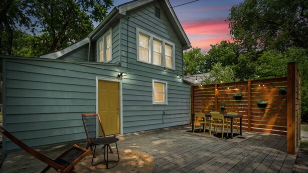 A house with a deck, a yellow door, and a wooden fence with lights.