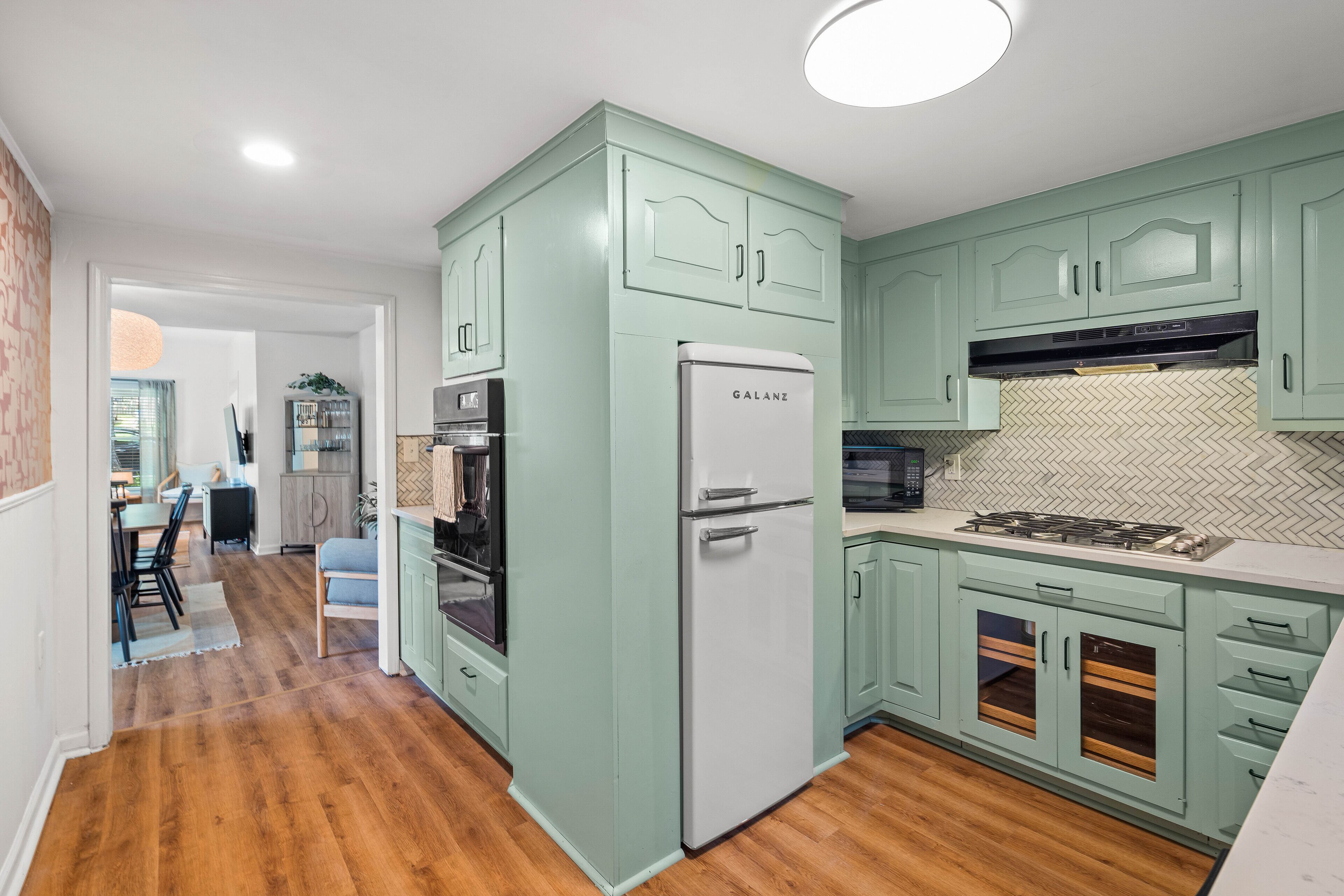 A modern kitchen with teal cabinetry, a white refrigerator, and a herringbone-patterned backsplash.