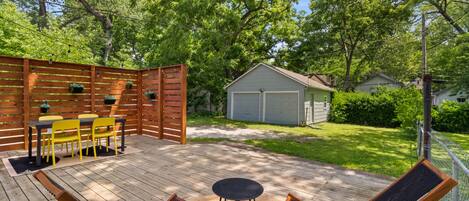 A wooden deck with a table and chairs, a small shed, and a fenced area with trees.