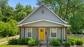 A small, single-story house with a yellow front door, a wooden porch, and a number "4443" on the door.