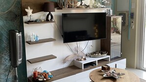 Ein modernes Wohnzimmer mit einem Flachbildfernseher an einer Holzwandverkleidung, einem Deckenventilator und einem rustikalen Couchtisch.
