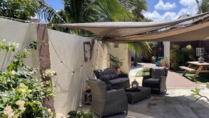 Ein Terrassenbereich im Freien mit Korbmöbeln, einem großen Pflanzgefäß und Topfpflanzen.