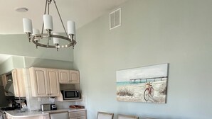 Ein Essbereich mit Holztisch und Stühlen, eine Küche im Hintergrund und ein Strandbild an der Wand.