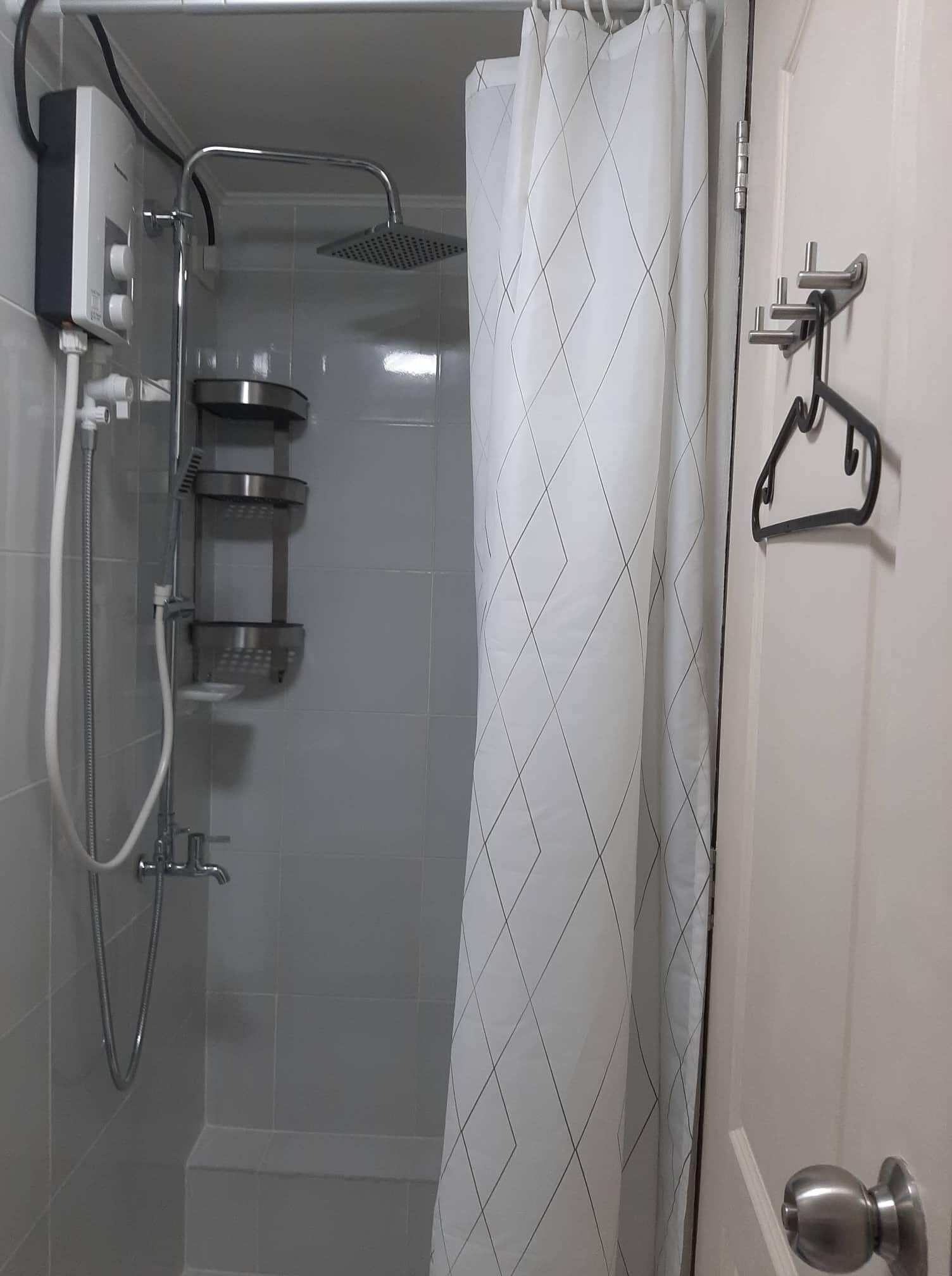 A shower area with a showerhead, handheld shower, and a wall-mounted control panel.