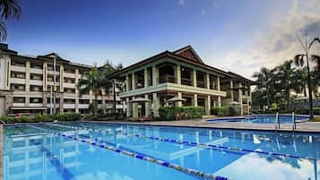 A swimming pool with clear blue water and lane dividers, surrounded by a building with multiple balconies and a tropical setting.