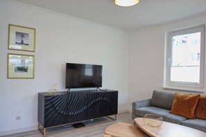 Una sala de estar moderna con un televisor de pantalla plana montado en un mueble oscuro y texturizado, un sofá gris con cojines marrones y una mesa de centro de madera.