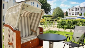 A wicker chair with a striped cushion and a small round table on a balcony. - Terrace, free use of the AHOI adventure pool and sauna - Sea view apartment 78 - (Göhren)