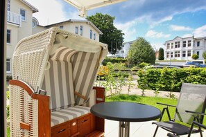 A wicker chair with a striped cushion and a small round table on a balcony.
