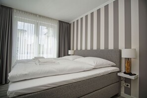 A hotel room with a large bed, two bedside lamps, and a view of the outdoors through sheer curtains. - Terrace, free access to the AHOI adventure pool and sauna - Apartment 78 with a view of the sea - (Göhren)