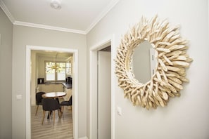 A hallway with a round mirror made of natural materials, a dining area with a round table and chairs, and a kitchen visible through an open door.