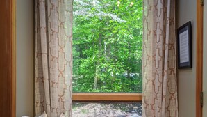 Un siège de fenêtre agrémenté de coussins à motifs, une vue sur la verdure à l’extérieur et un avis encadré accroché au mur.