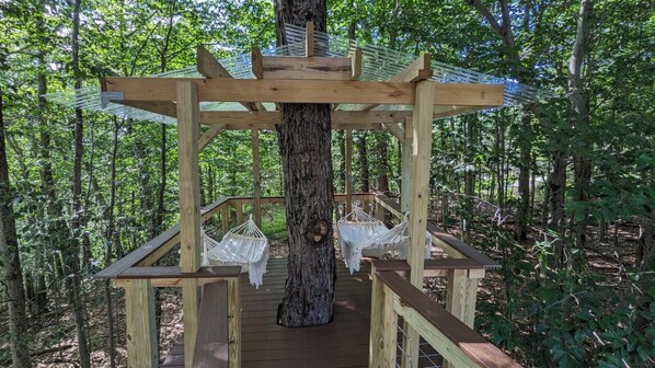 Una casa en árbol de madera con un columpio de cuerda y una hamaca, rodeada por un bosque.
