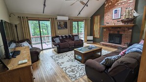 Un salon spacieux avec une cheminée, un balcon offrant une vue sur les arbres et une grande fenêtre.