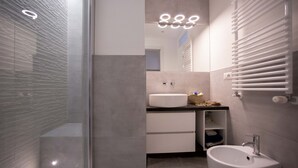 A modern bathroom with a glass shower enclosure, a white sink, and a vanity with drawers and a mirror. - GetTheKey Monte Ceneri Apartment (Milano)