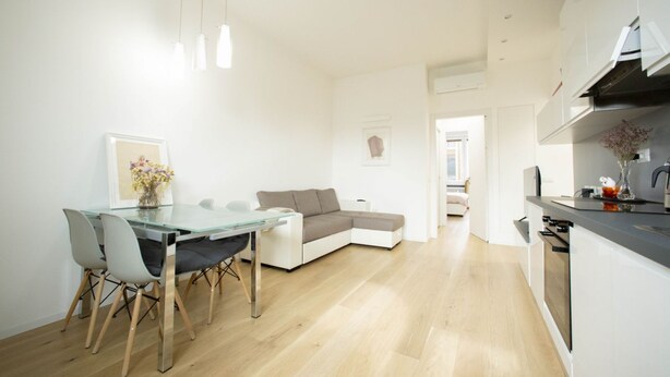 A modern kitchen with white cabinets, a dining area with a glass table and chairs, and a grey sofa. - GetTheKey Monte Ceneri Apartment (Milano)