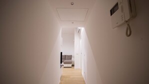 A narrow hallway with a wooden floor leading to a room with a bed and a white wall-mounted phone. - GetTheKey Monte Ceneri Apartment (Milano)