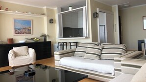 A living room with a sofa, a coffee table, a chair, a kitchen area, and a painting on the wall. - Amazing sea view near Barcelona (Sant Pol de Mar)