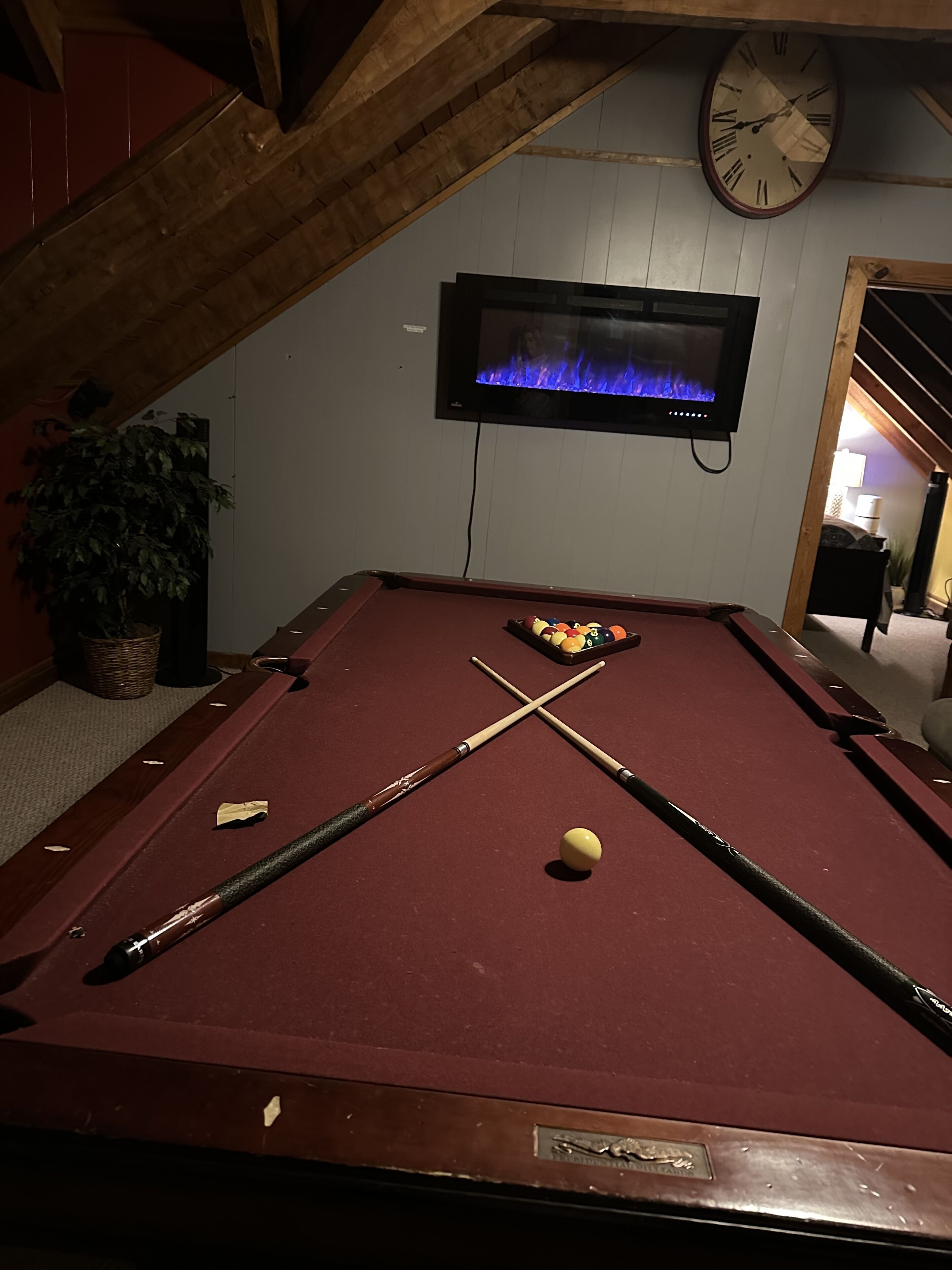 A pool table with cues and balls, a television displaying a fireplace, and a clock on the wall.