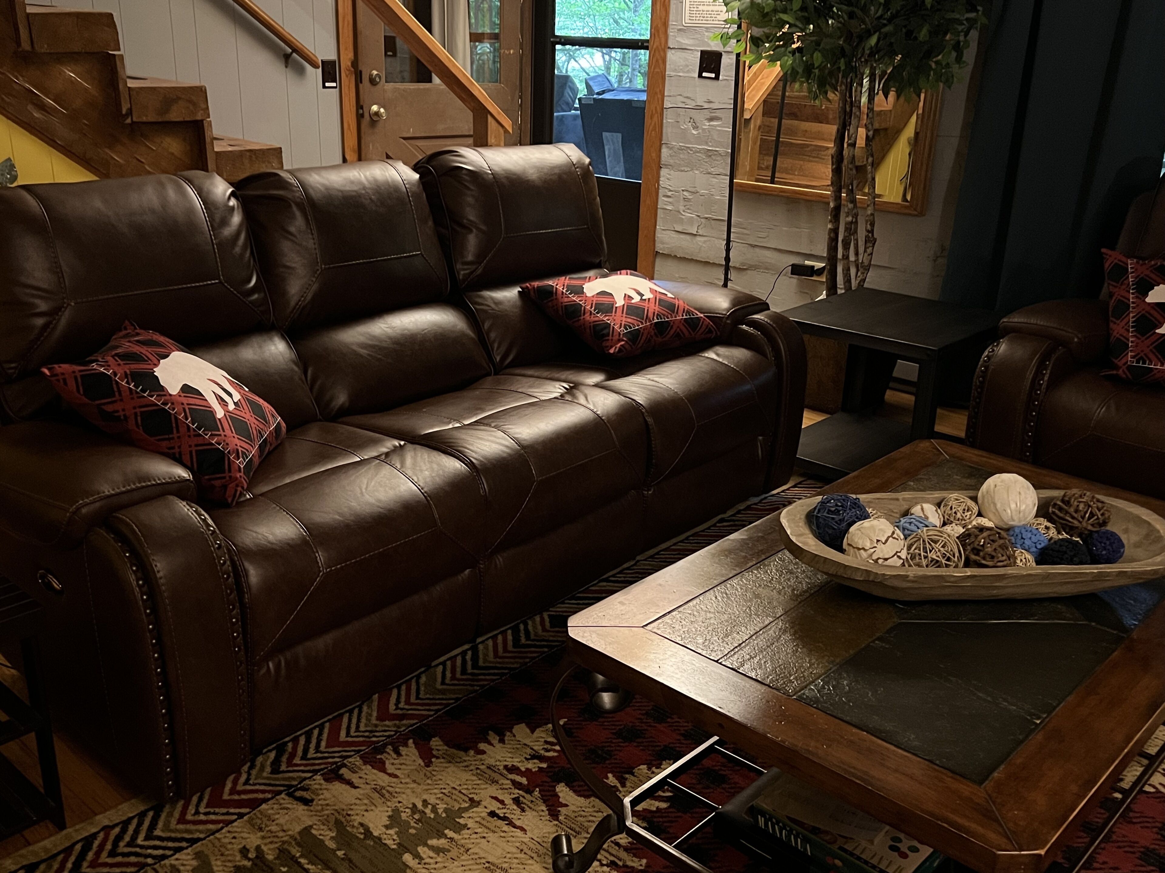 A brown leather sofa with patterned cushions, a coffee table with decorative items, and a patterned rug.