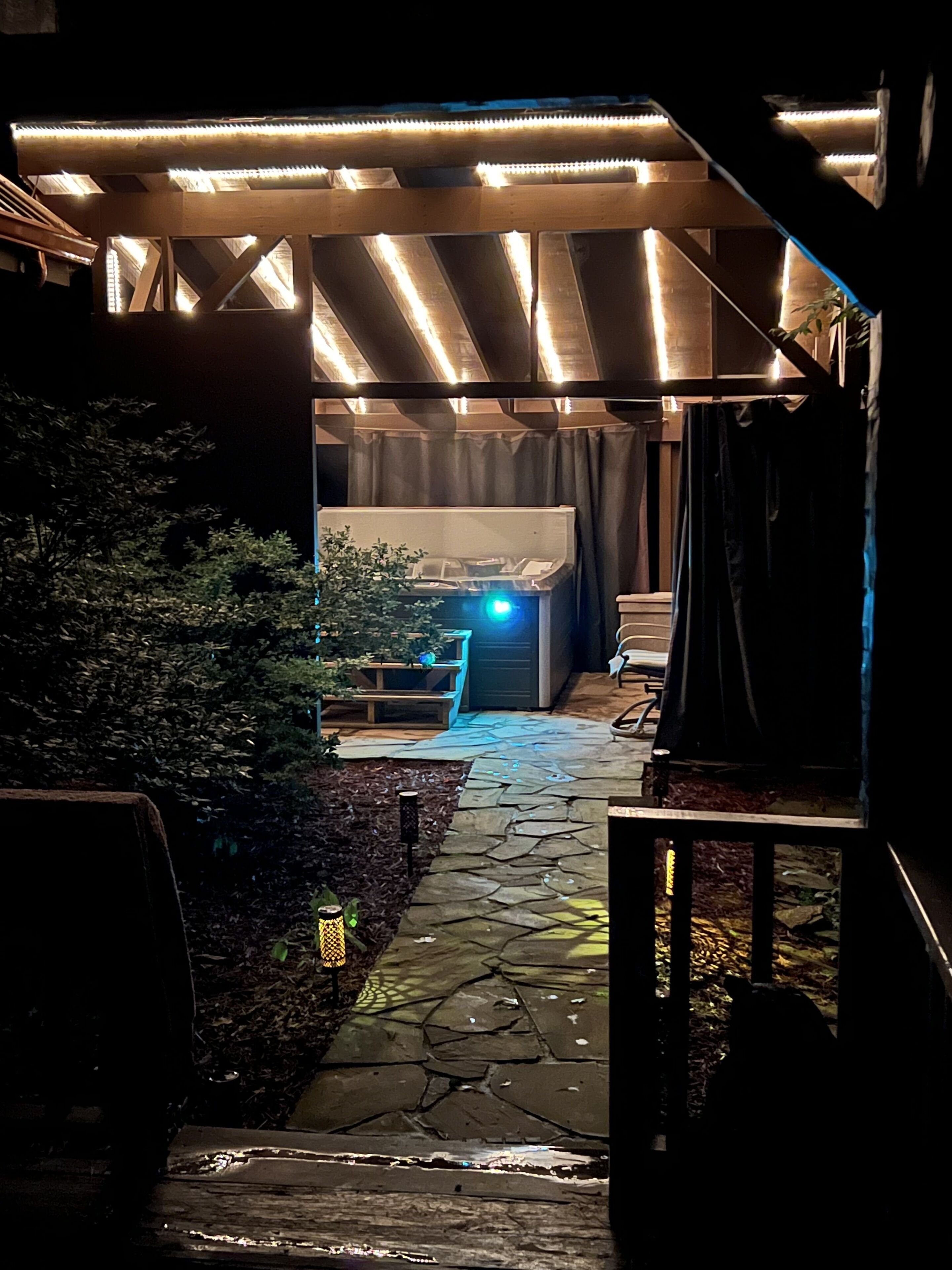 Un sentier mène à un espace extérieur abrité, aménagé avec un lit et un bureau.