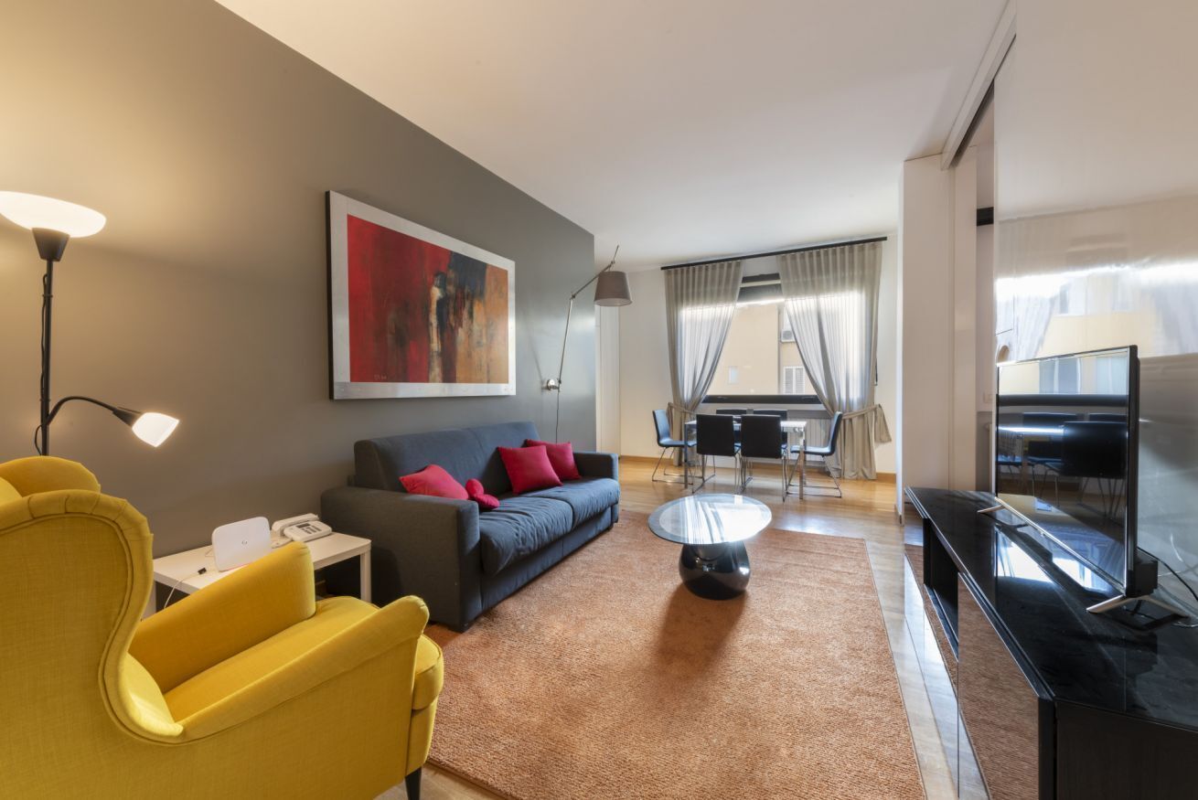 Ein modernes Hotelzimmer mit einer Couch, einem gelben Sessel, einem Couchtisch, einem Fernseher und einer Essecke.