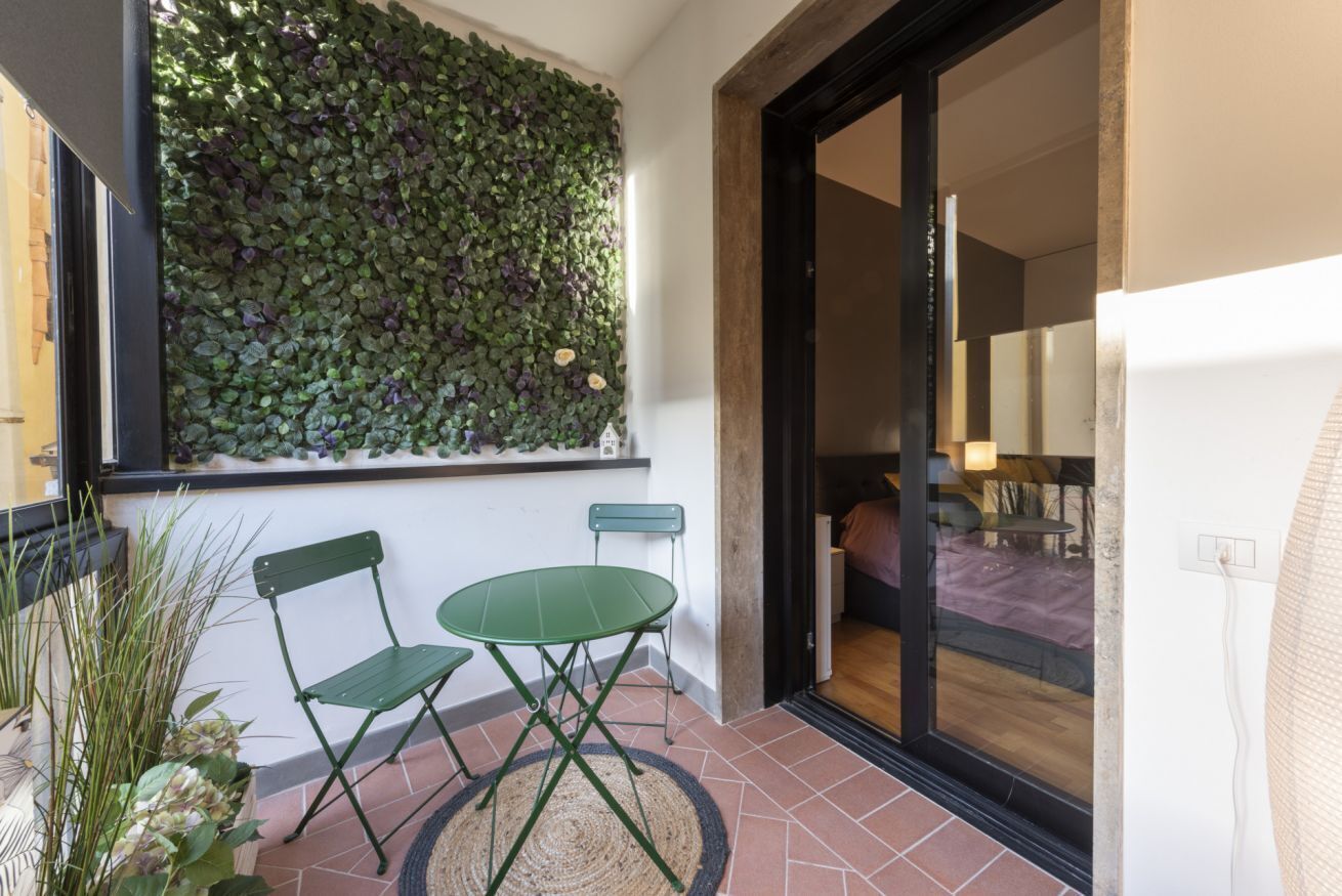 A balcony with a green metal table and chairs, a potted plant, and a wall-mounted plant display.