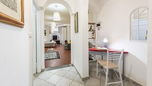 Um corredor com um arco que dá para uma sala de estar, uma mesa com uma cadeira e uma janela.