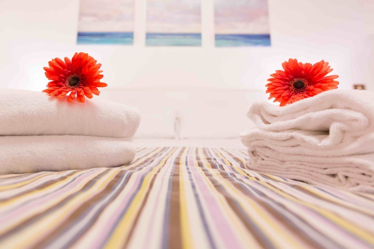 Un lit bien fait, avec une literie à rayures et deux fleurs rouges posées sur des serviettes pliées.