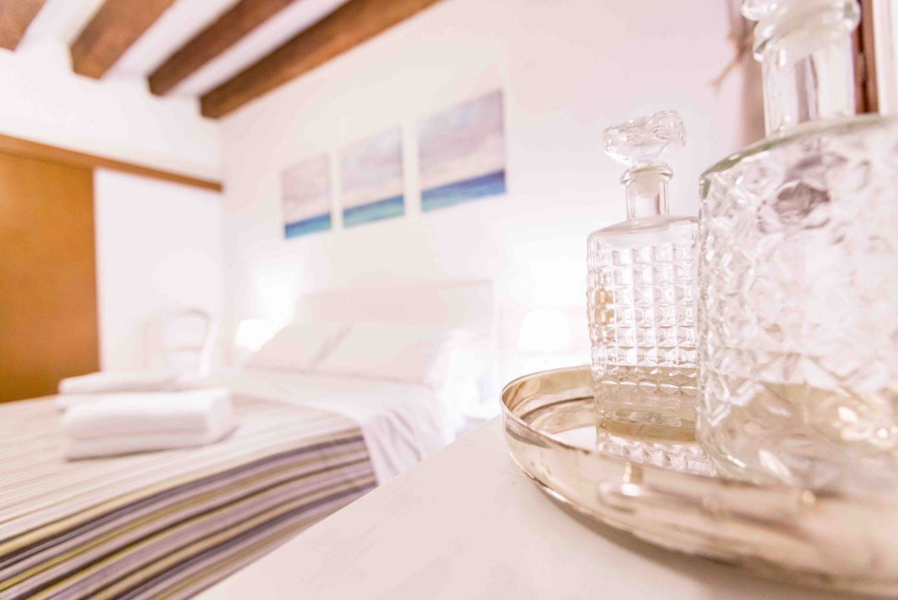 A hotel room with a bed, a tray with two crystal decanters, and a painting on the wall.