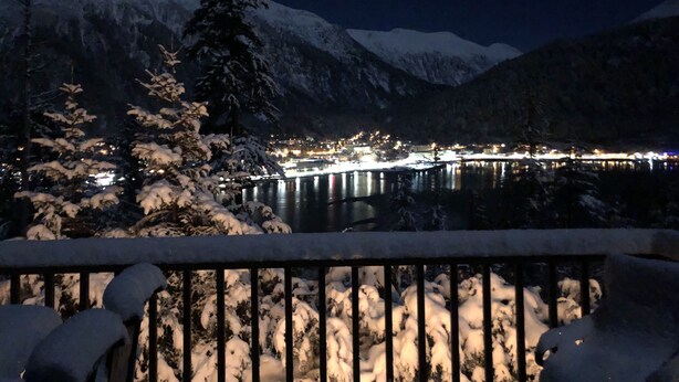 A snowy mountain landscape at night with a lit bridge and buildings in the background. - HIlltop Haven (Juneau)