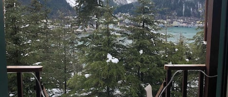A view from a balcony with wooden railings, overlooking a snow-covered landscape with mountains and a body of water.