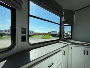 Enjoy a view of the surrounding area from the motorhome's windows, which offer a glimpse of the parking area and grassy field.