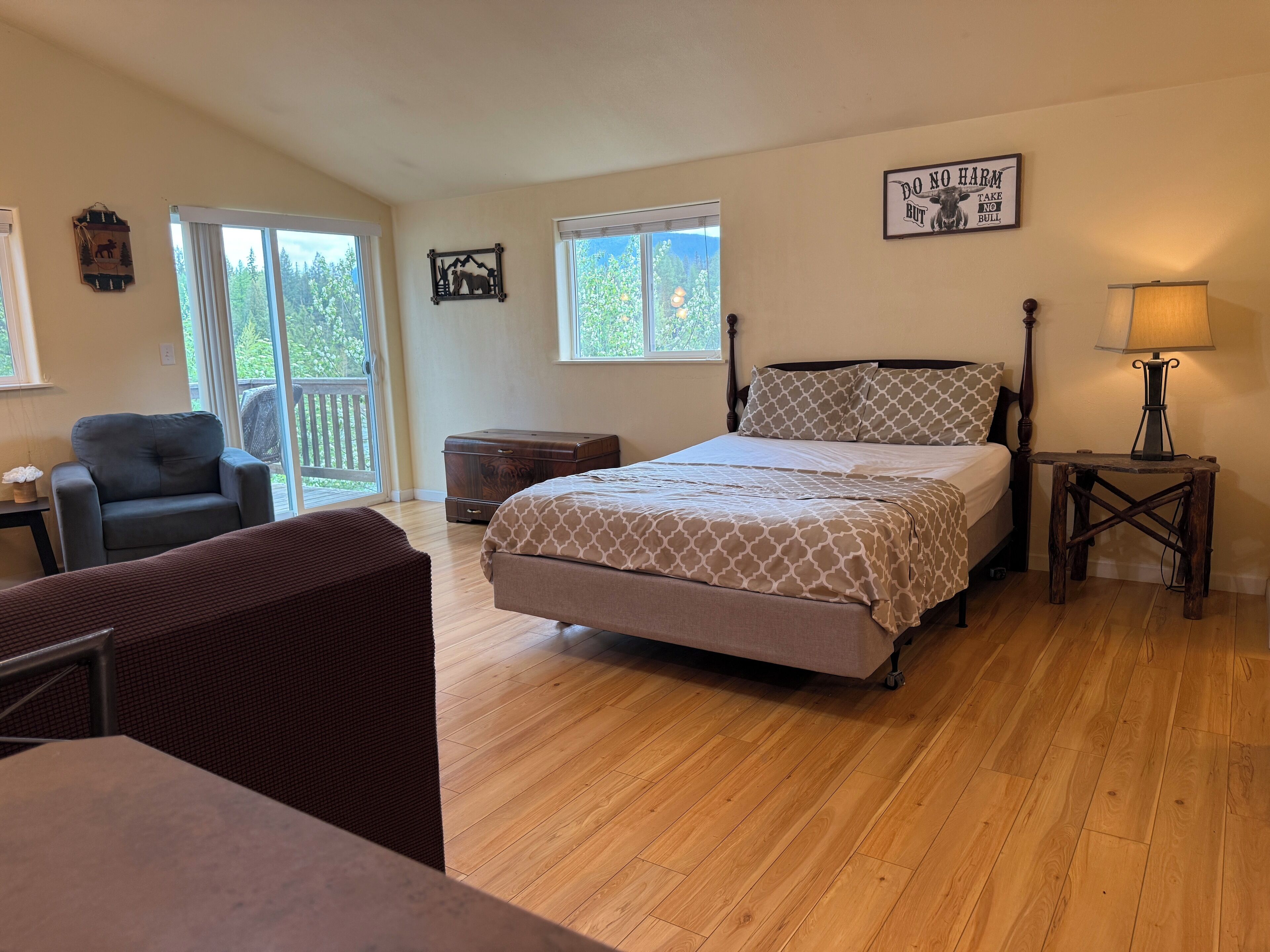 A bedroom with a bed, a chair, a dresser, a lamp, and a window with a view of trees.