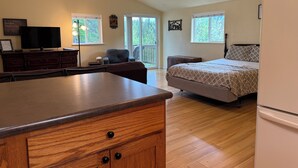 Une chambre spacieuse avec un grand lit, une commode en bois, une télévision et un balcon donnant sur un paysage verdoyant.