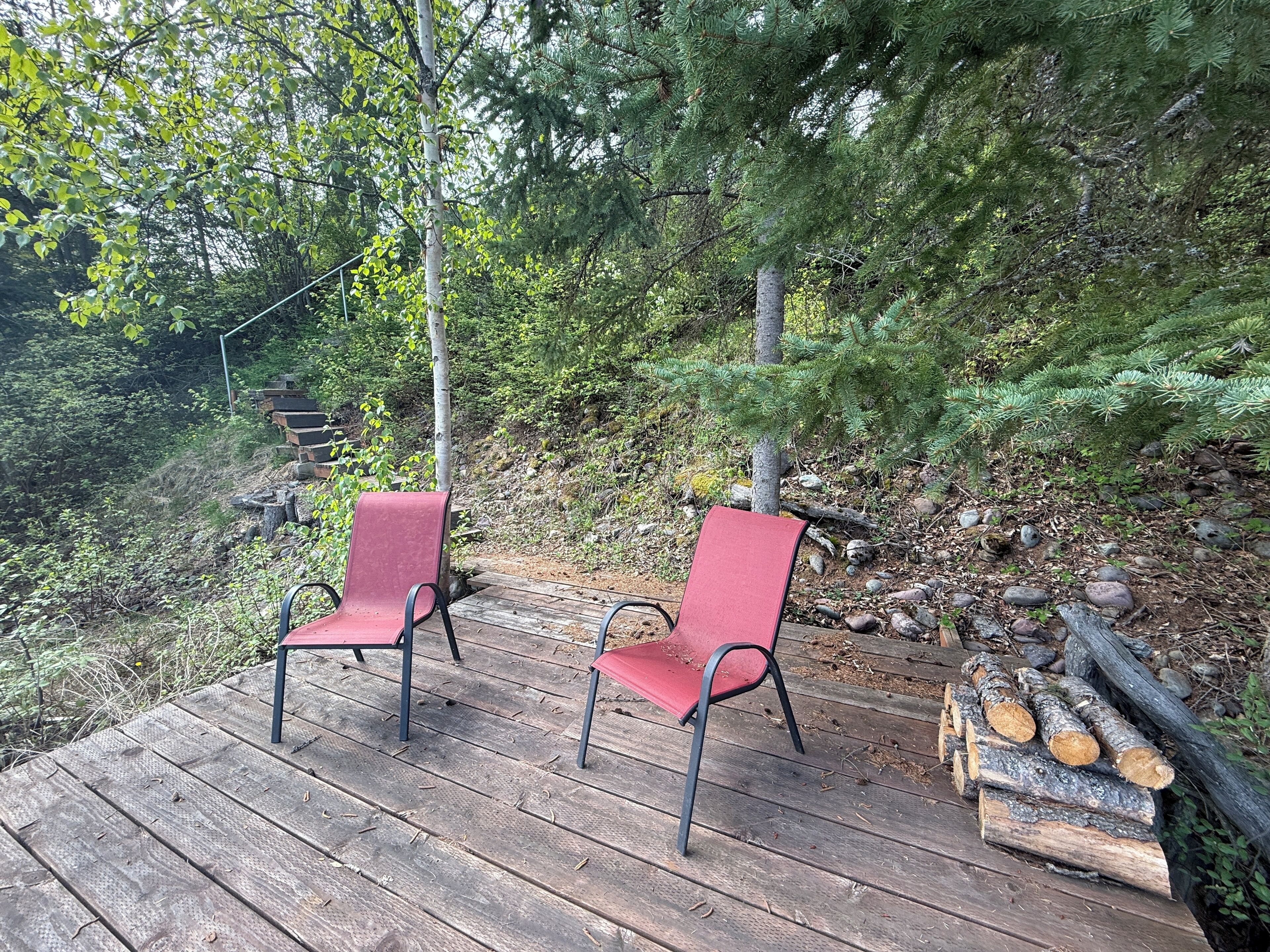 Eine Holzterrasse mit zwei roten Stühlen und einem Holzstapel.