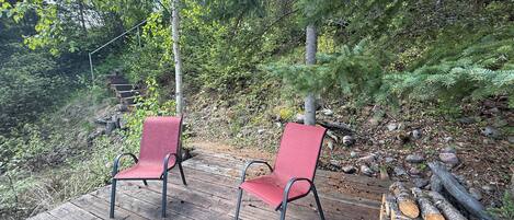 A wooden deck with two red chairs and a stack of firewood.