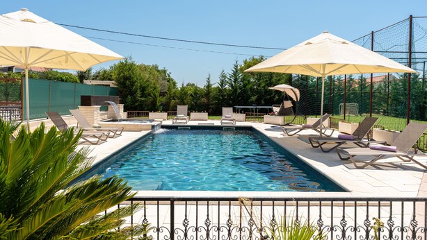 Una piscina amb gandules i para-sols, envoltada per una tanca i vegetació.